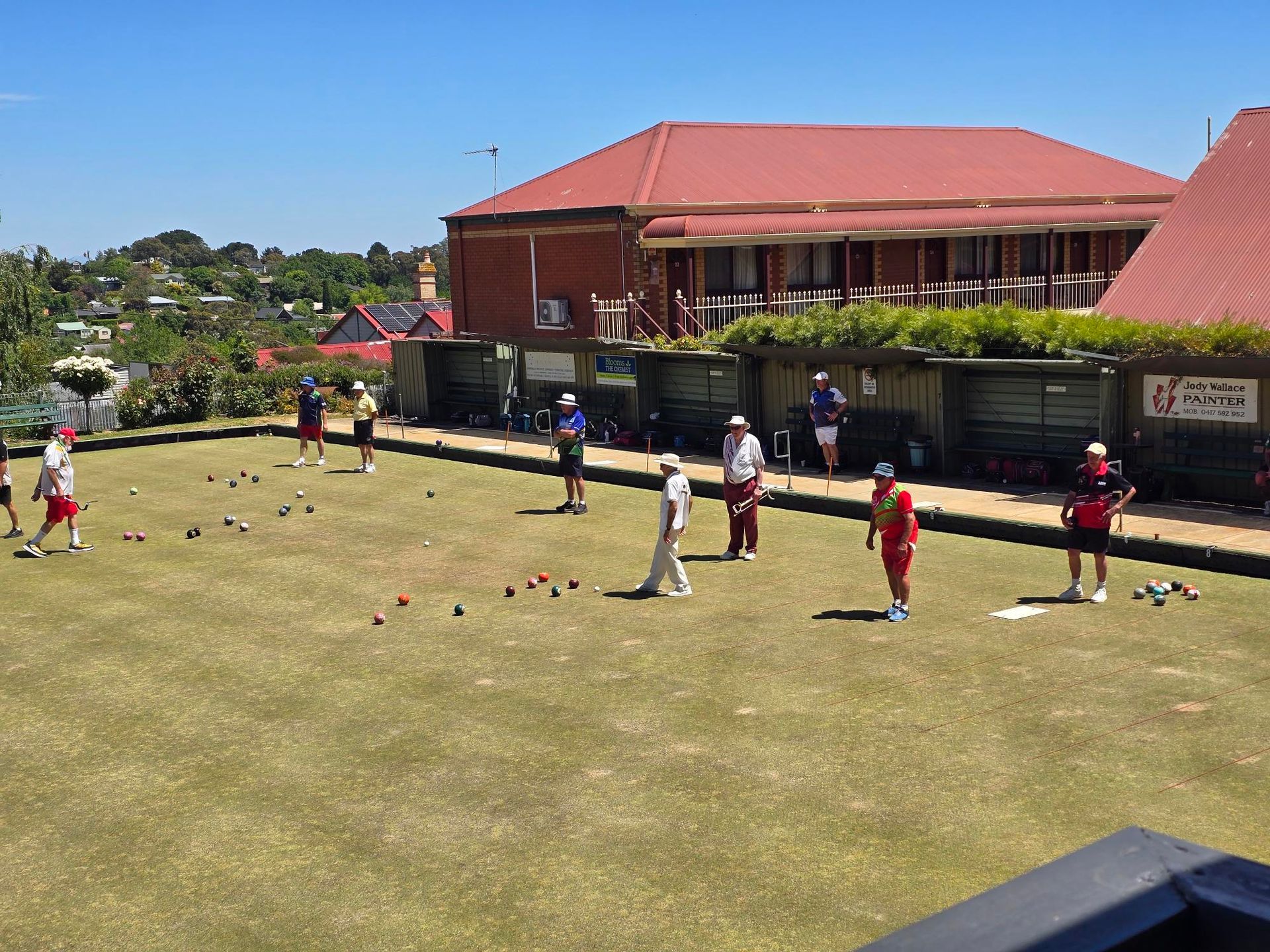 People playing lawn bowls on a sunny day. They have red and white uniforms.