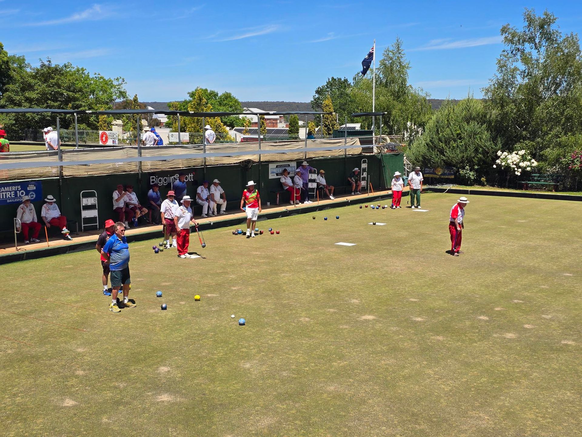 People playing lawn bowls on a sunny day. They have red and white uniforms.