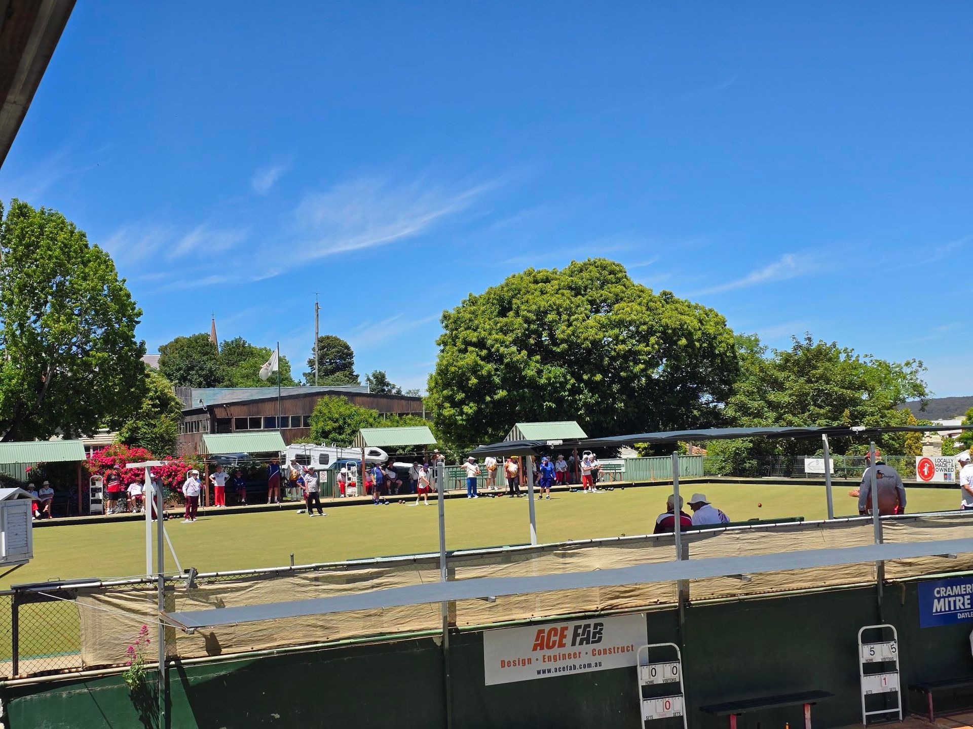 People playing lawn bowls on a sunny day. They have red and white uniforms.