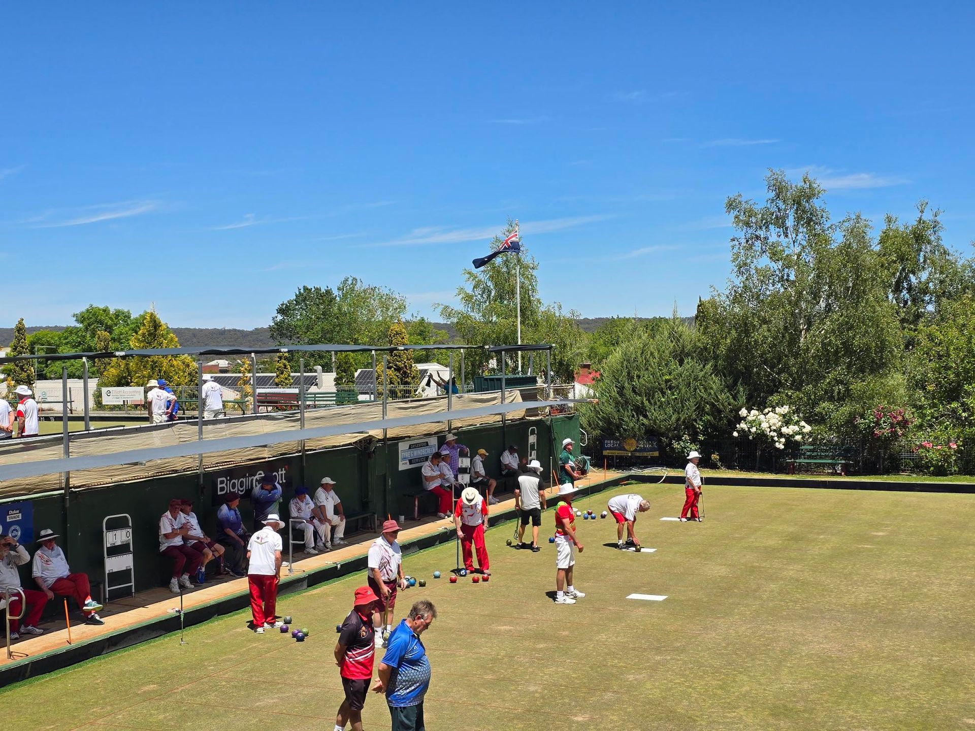 People playing lawn bowls on a sunny day. They have red and white uniforms.