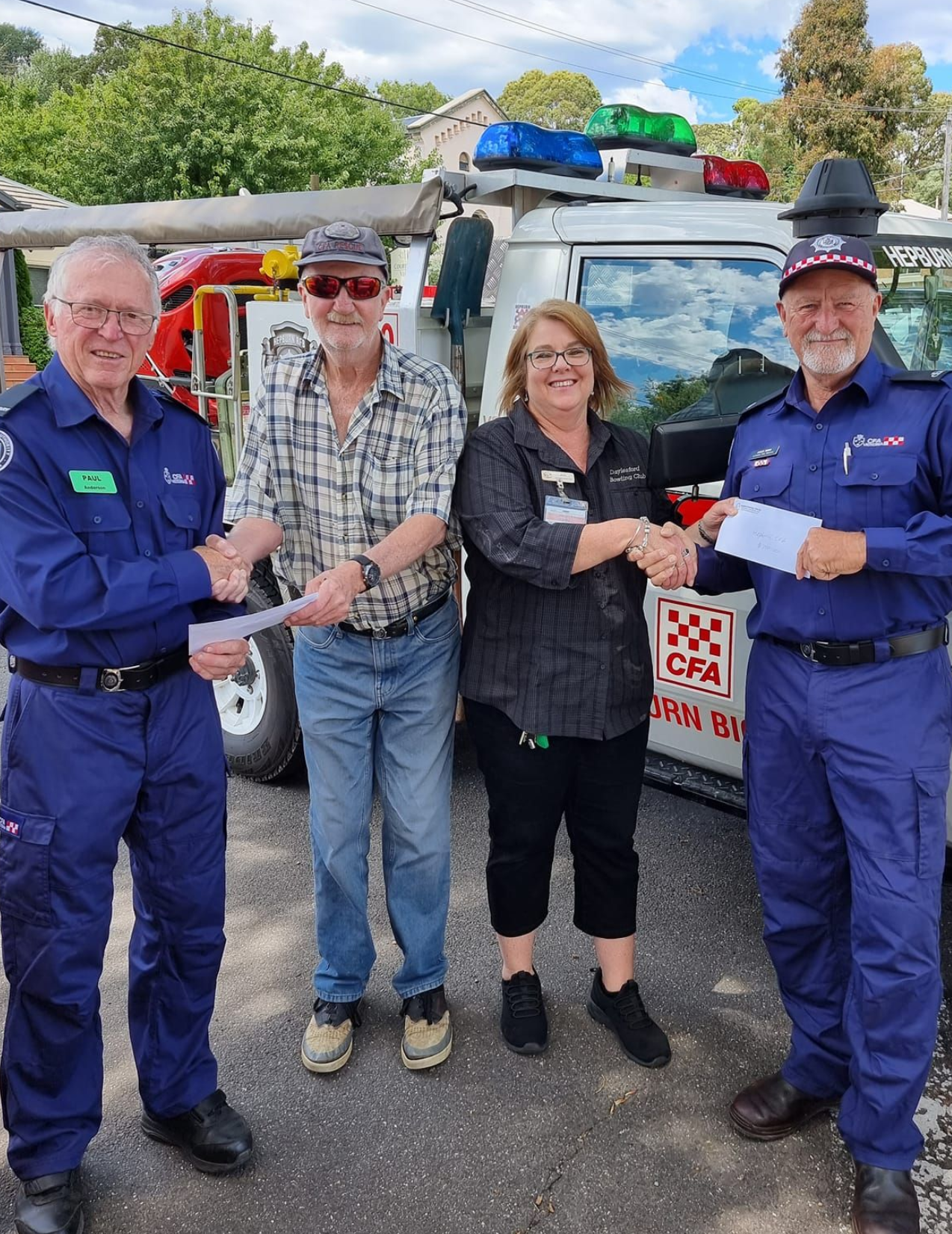 Picture of 4 people shaking hands in front of a fire truck. Two are in a blue uniform.