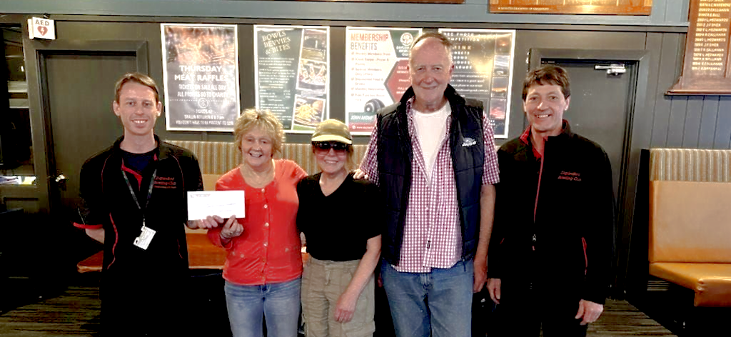 Five people lined up in a row for a photo opportunity. One person holding up a big cheque.