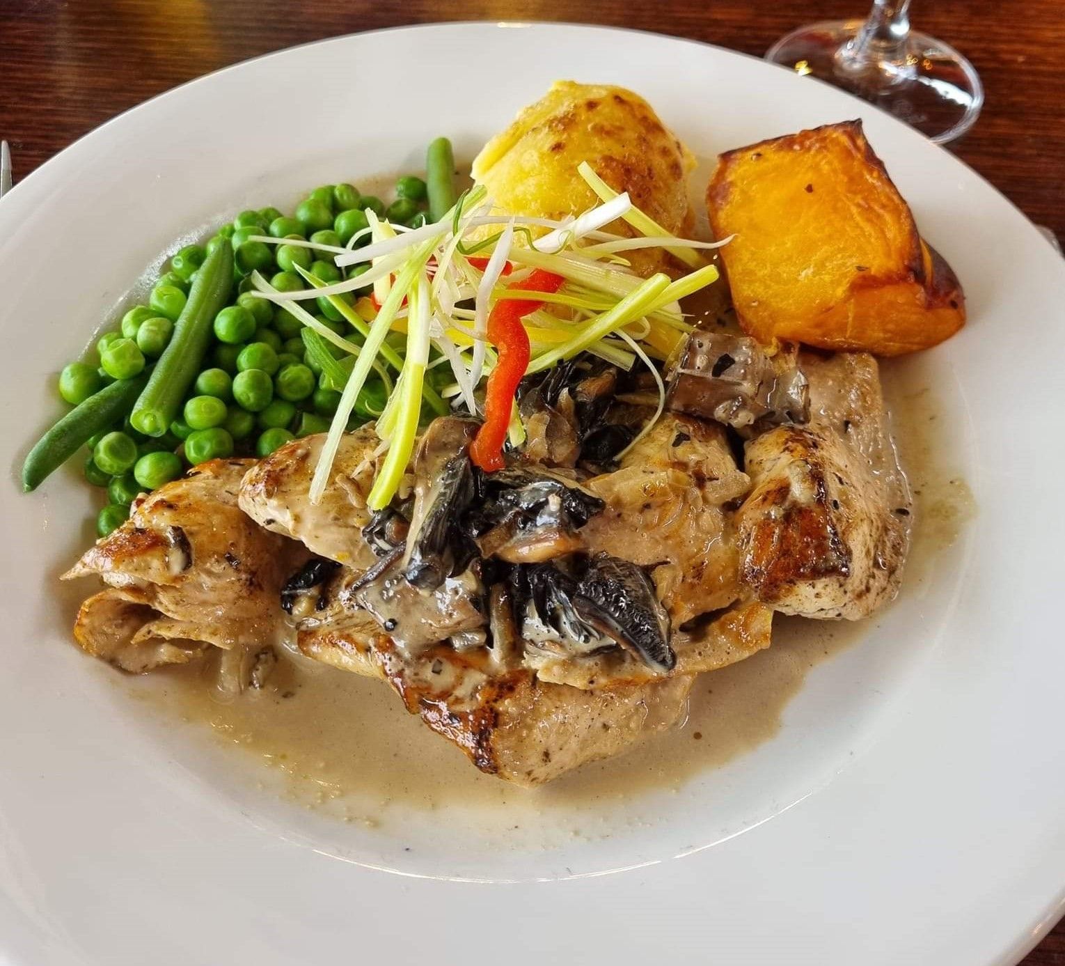 Plate of chicken with green peas and roast vegetables.