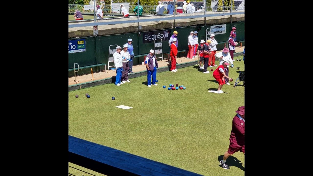 People playing lawn bowls on a sunny day. They have red and white uniforms.