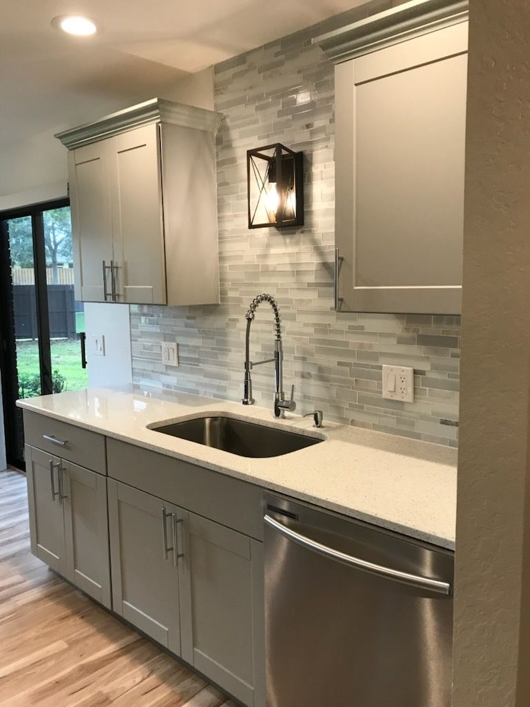 Modern kitchen with gray cabinets, white countertops, subway tile backsplash, and stainless steel sink.