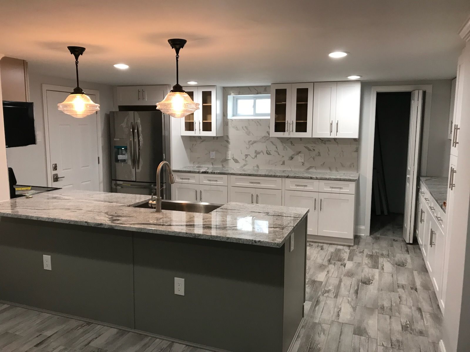 Modern kitchen with dark island, white cabinets, granite counters, stainless fridge, and gray flooring