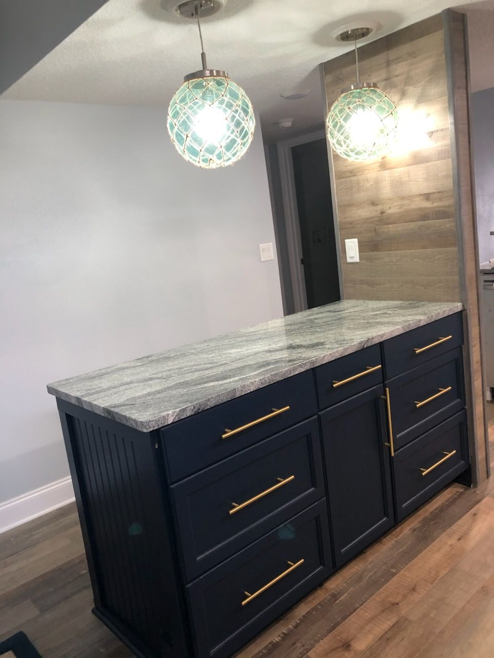 Dark kitchen island with gray marble top, navy cabinets, and two green pendant lights in a modern room