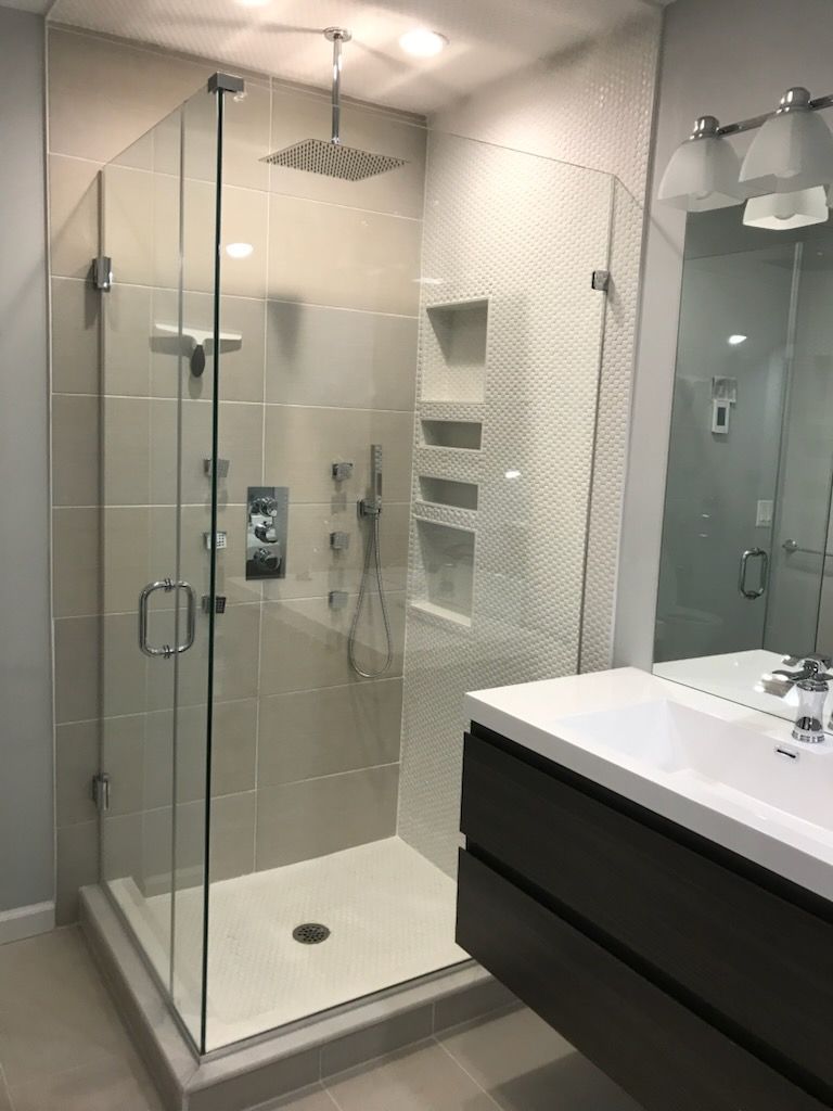 Modern bathroom with glass walk-in shower, rainfall showerhead, and dark vanity beside a sink.