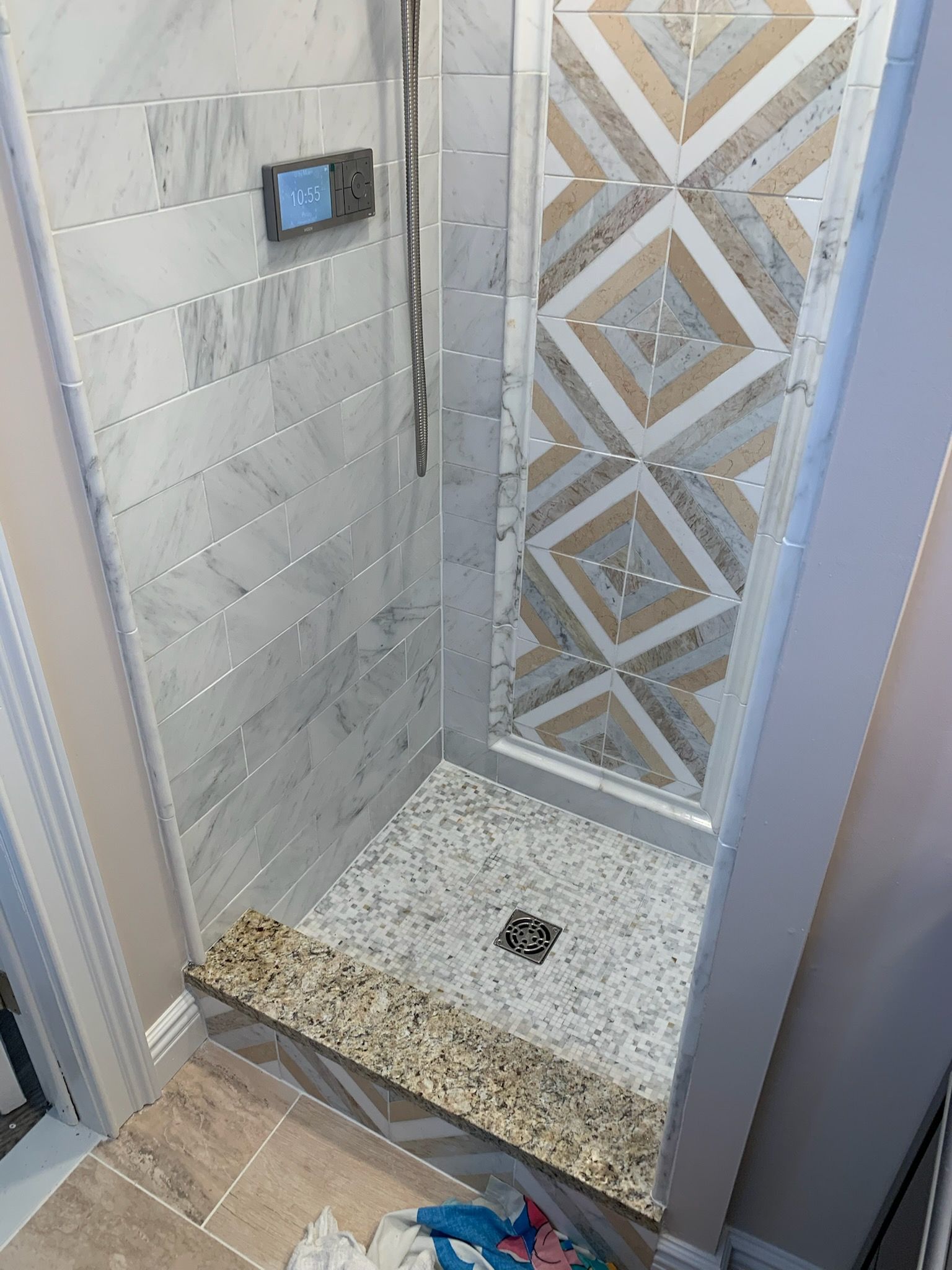 Small tiled shower stall with a glass door, gray-and-white walls, and a pebble shower floor.