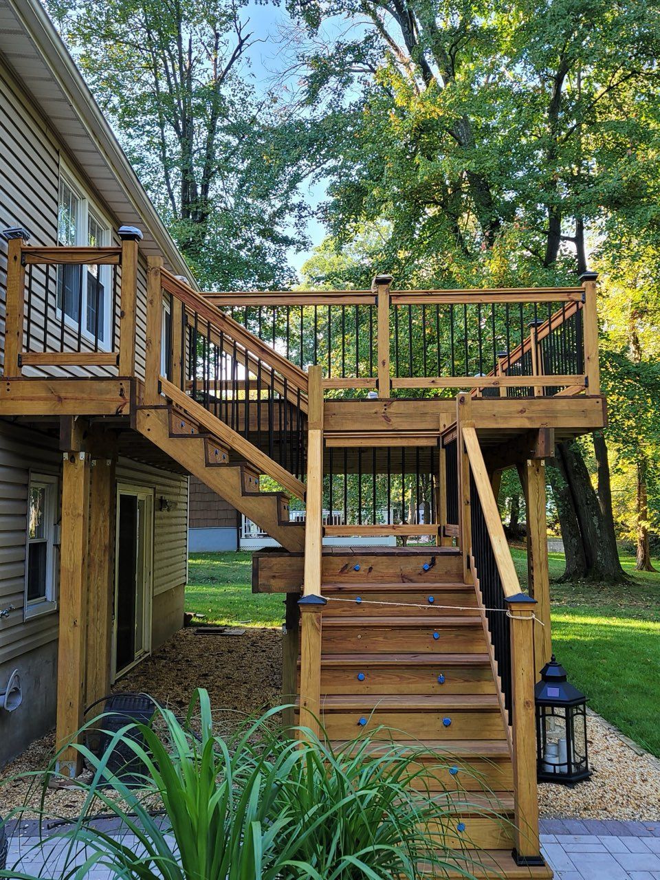 Wooden outdoor deck stairs beside a house, with a railing and lantern in a leafy backyard.