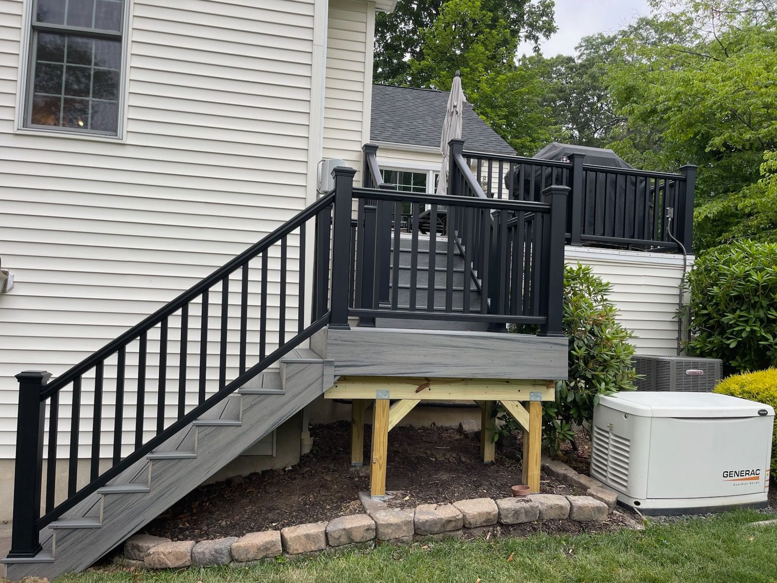 Black staircase and deck attached to a house, with support posts and an air conditioner unit below.