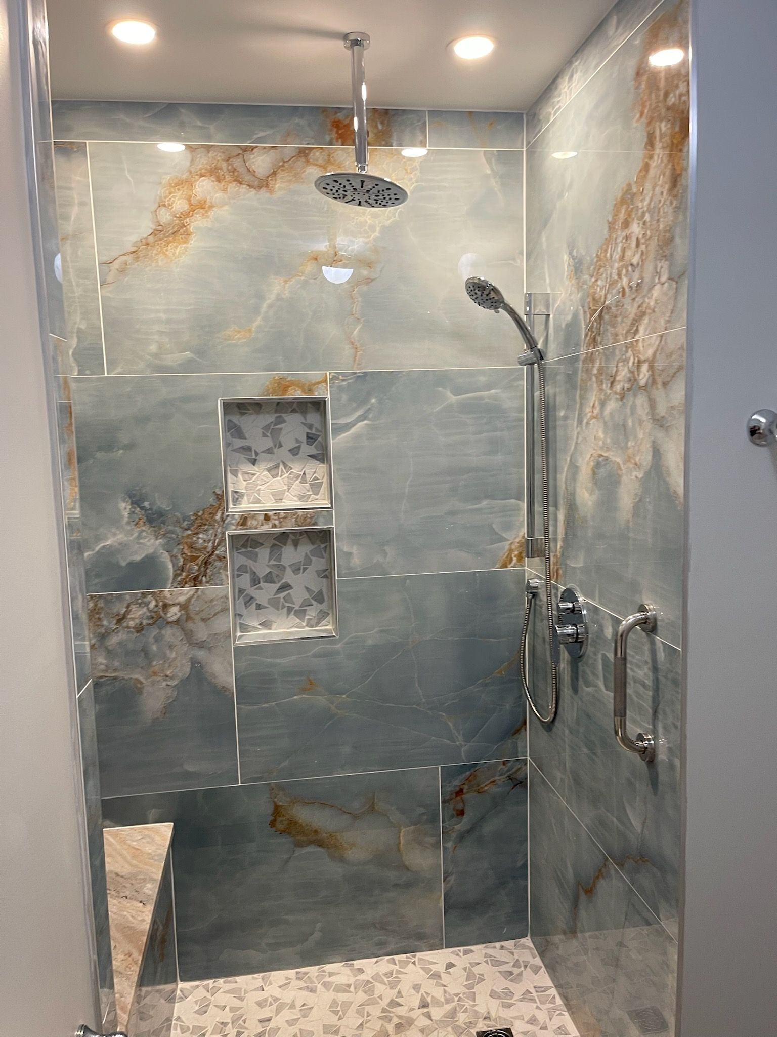 Modern tiled shower with built-in niche, rain showerhead, and glass door harnesses