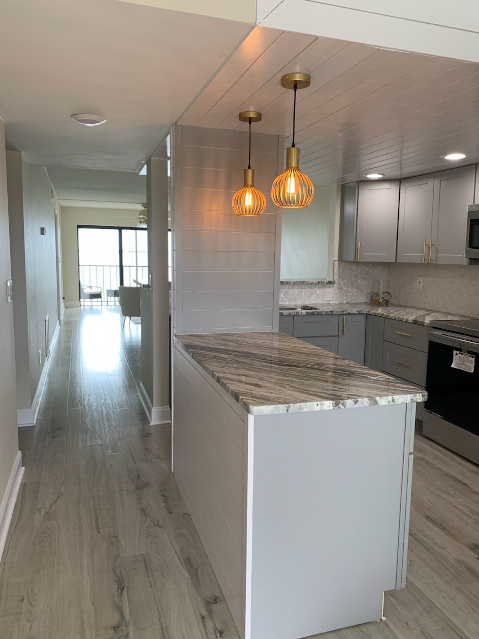 Bright modern kitchen with marble island, pendant lights, and hallway opening to a sunlit room