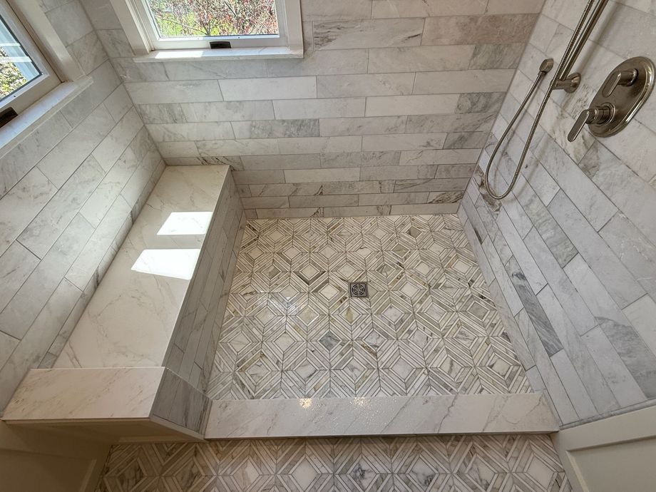 White tiled walk-in shower with a built-in bench, patterned floor, and two windows.