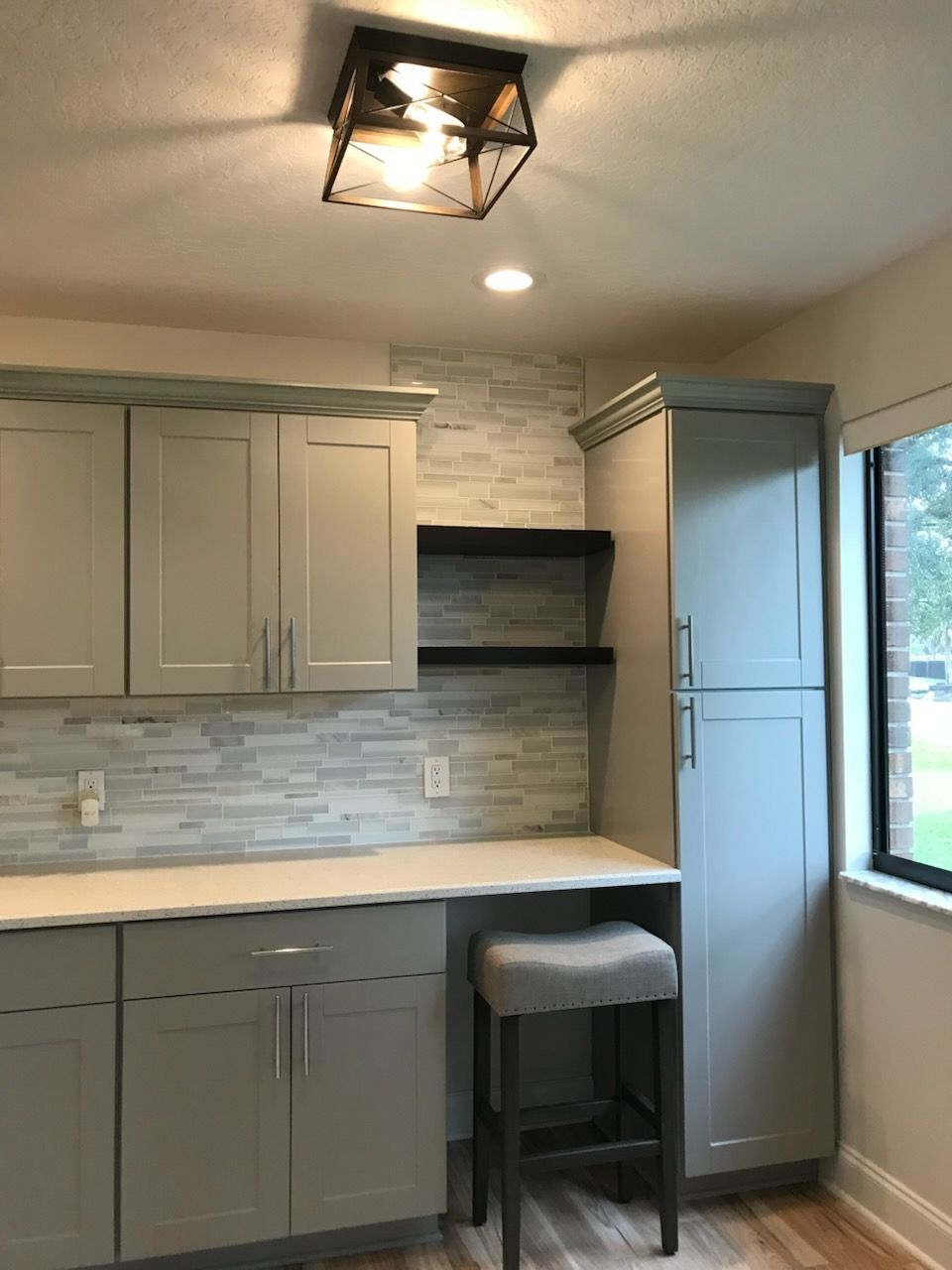 Small modern kitchen with gray cabinets, white countertop, tiled backsplash, and a window.