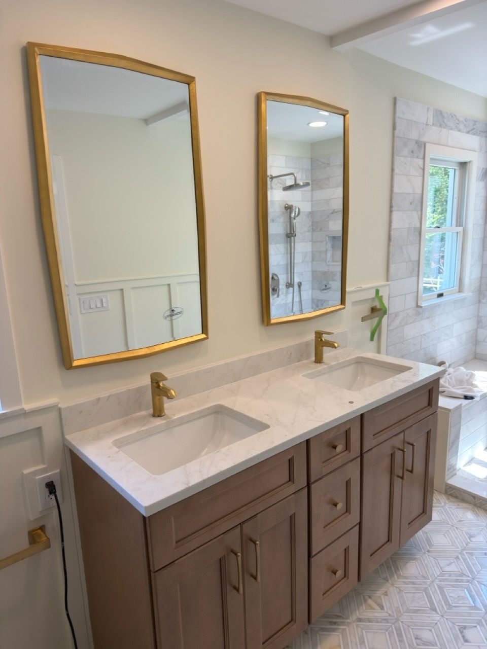 Modern bathroom vanity with double sinks, brass faucets, mirrors, and marble countertop under bright natural light