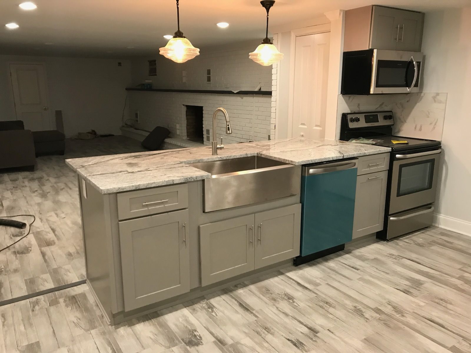 Modern kitchen island with marble countertop and sink, stainless stove, gray cabinets, and blue dishwasher; living room beyond