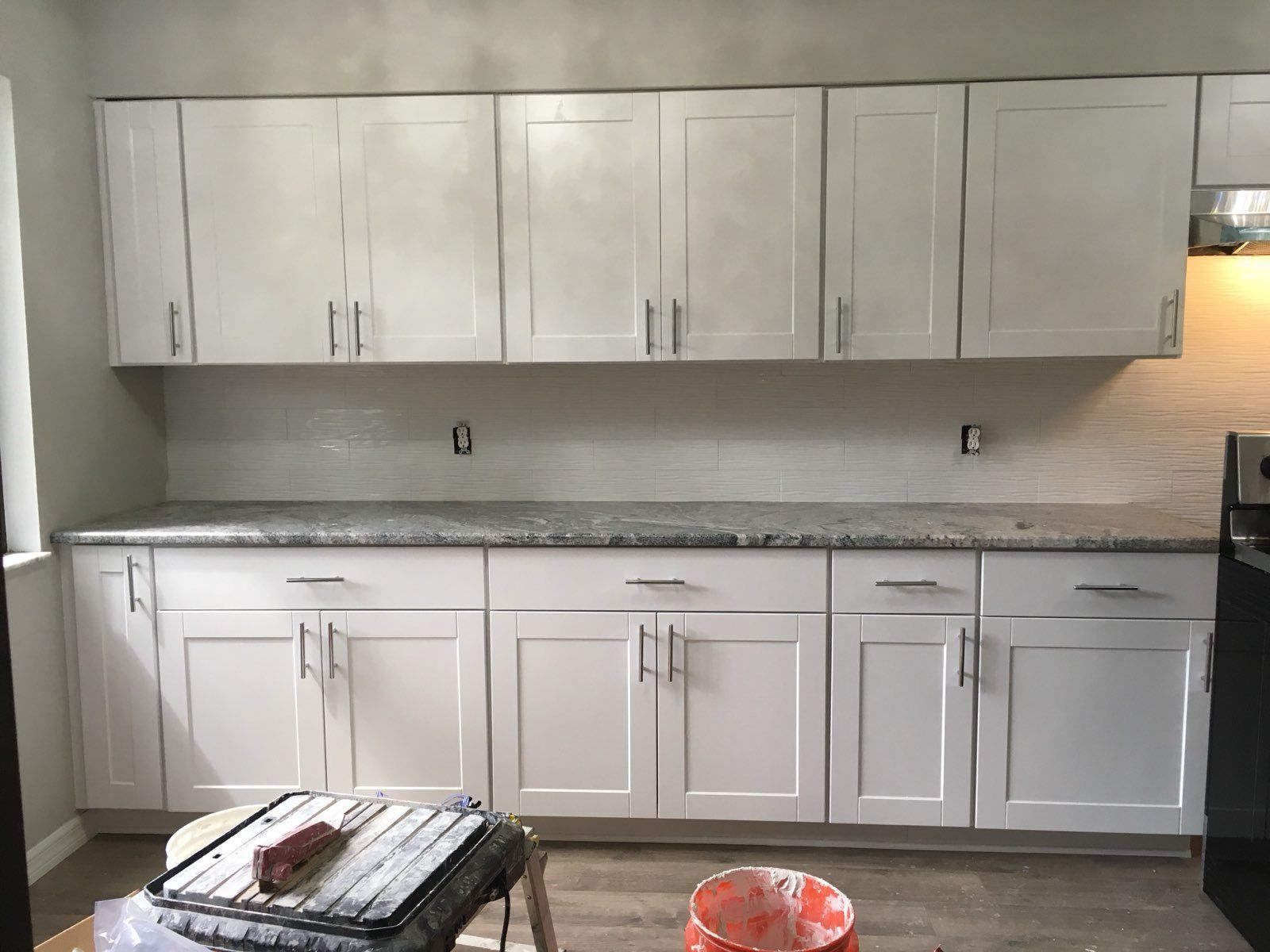 Bright white kitchen with upper and lower cabinets, gray countertop, and a small table in the foreground