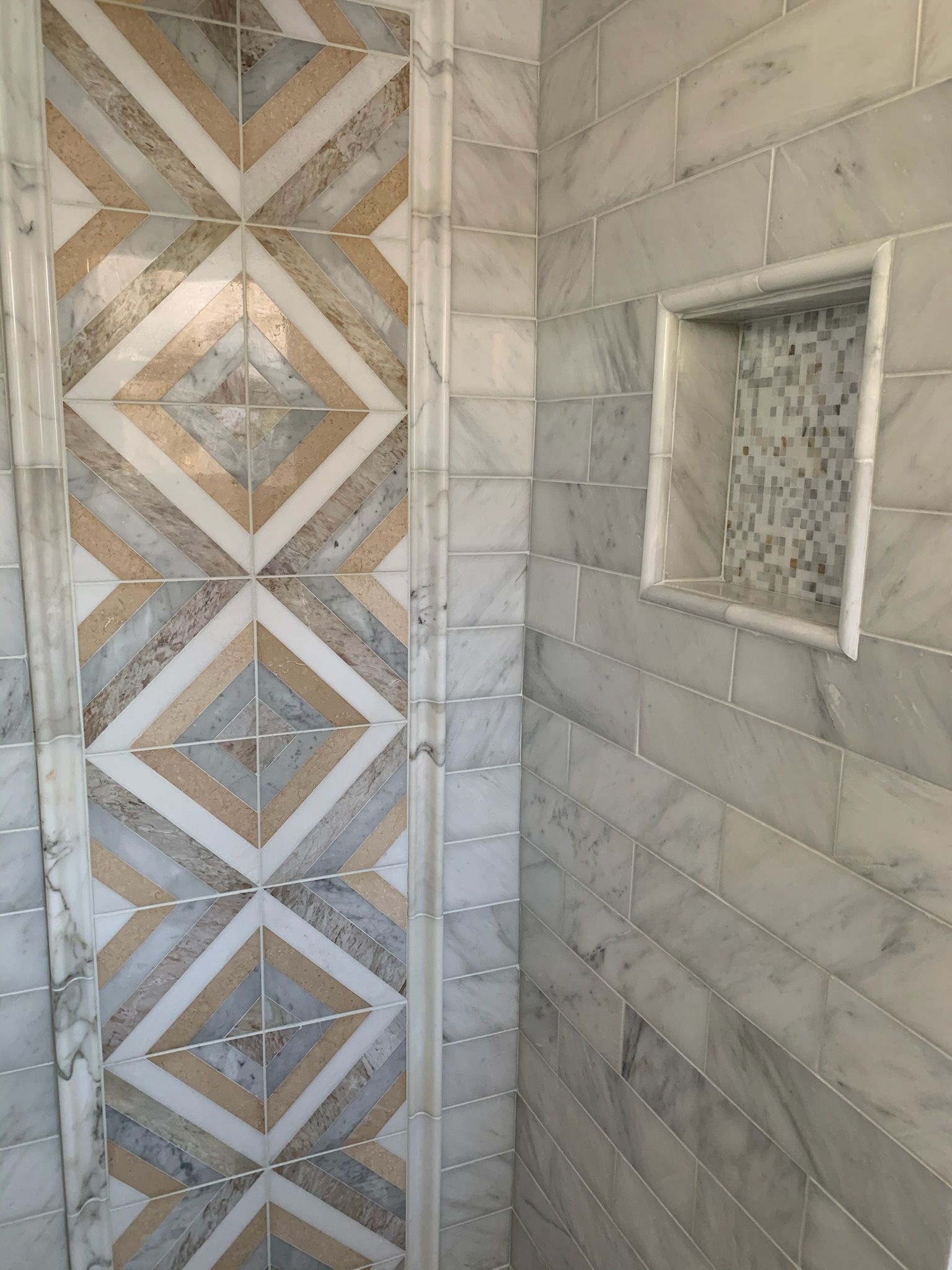 Decorative tiled shower wall with tan, gray, and white geometric patterns and a small recessed shelf