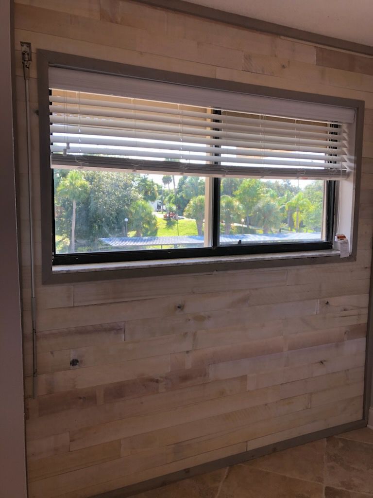 Wood-paneled room wall with a horizontal window and partially open blinds, showing trees outside.