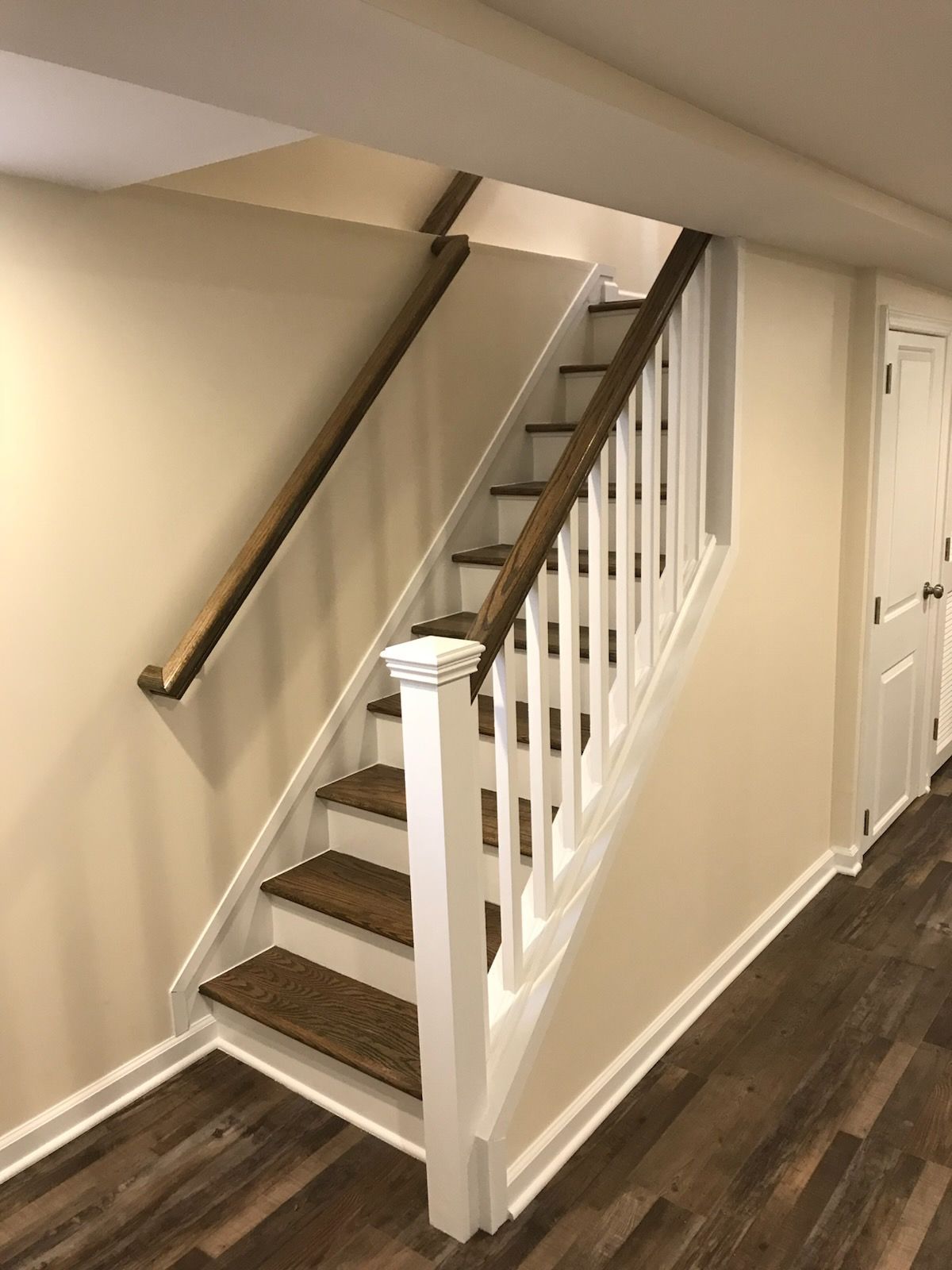 Indoor staircase with white railing, brown carpeted steps, and dark wood flooring under a sloped ceiling