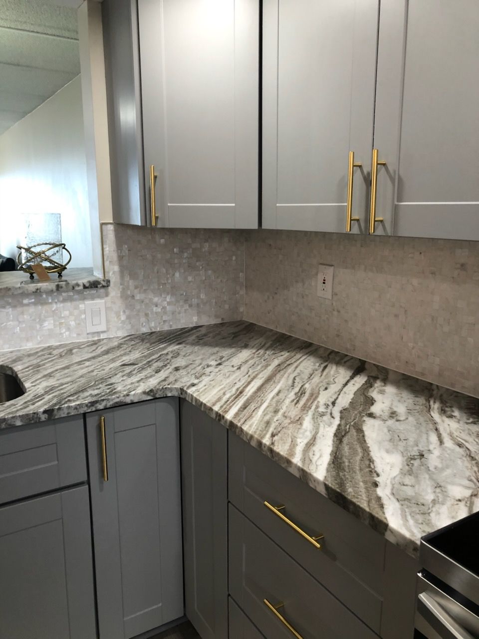 Gray kitchen corner with marble countertop, gray cabinets, and gold handles