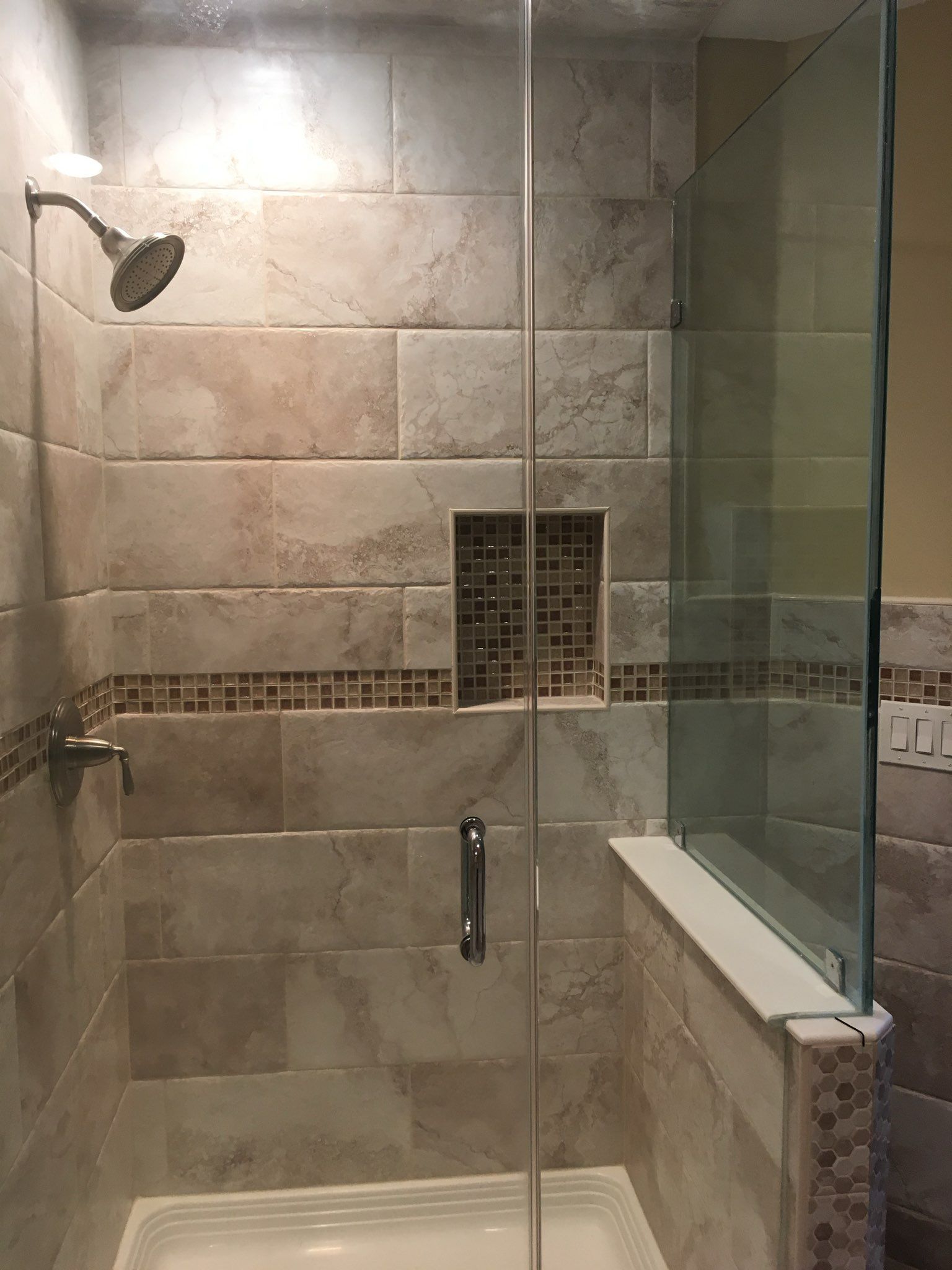 Tiled shower with glass door, wall-mounted showerhead, and built-in niche and shelf.