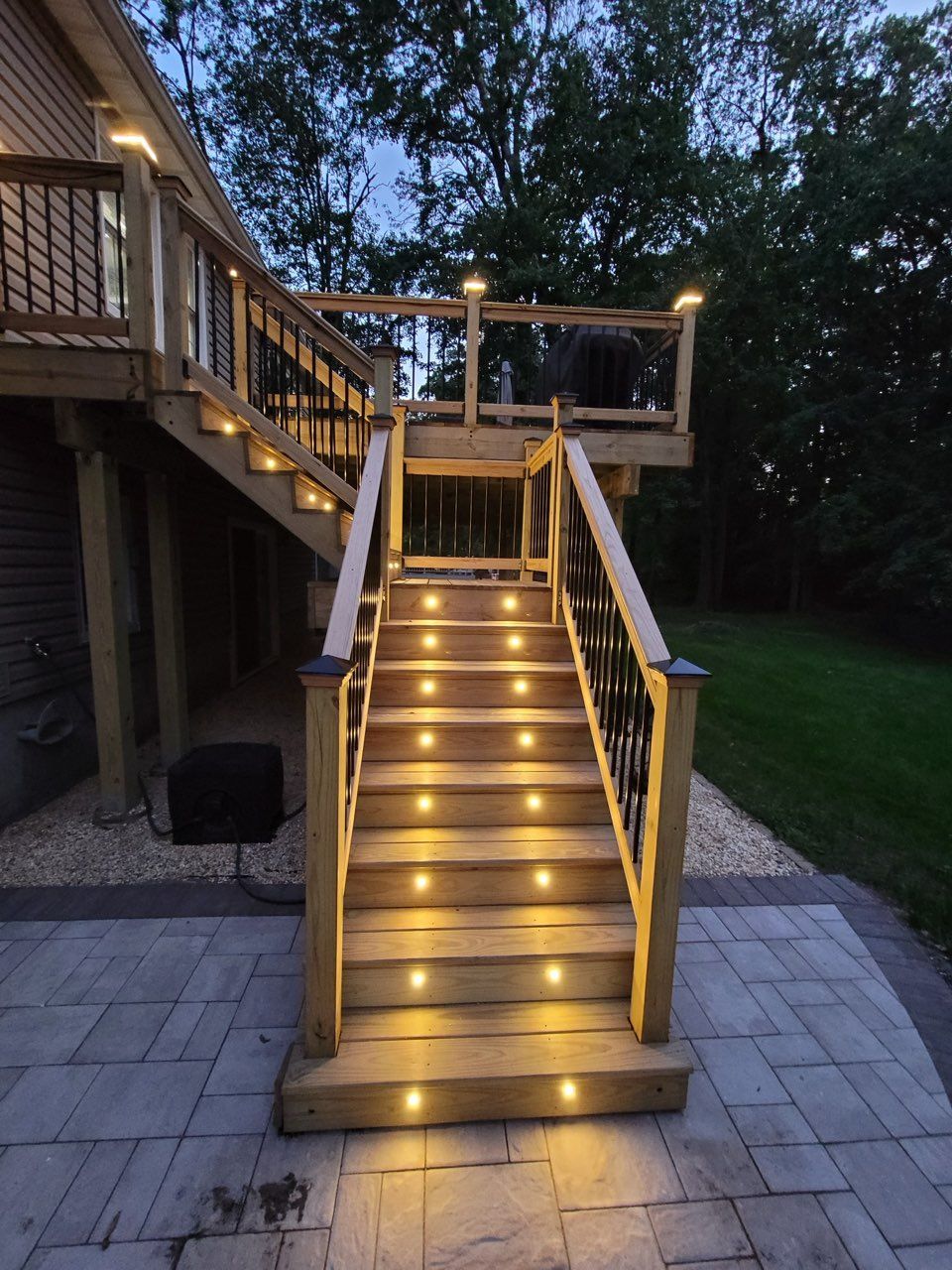 Illuminated outdoor wooden staircase with string lights leading to a deck at dusk