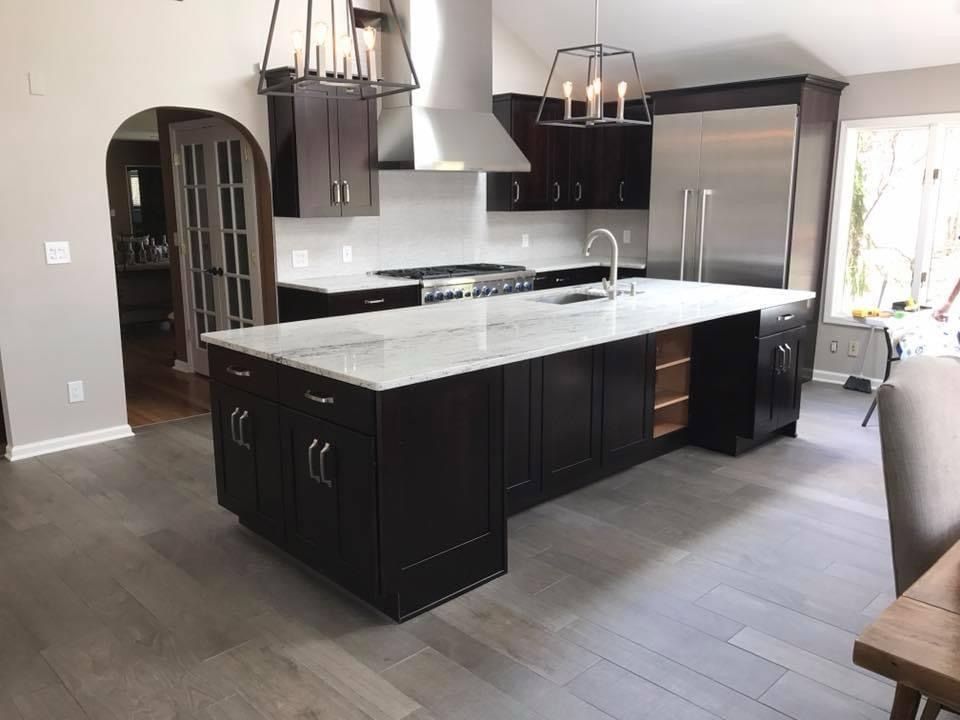 Modern kitchen with dark cabinets, white marble island, stainless steel appliances, and pendant lights