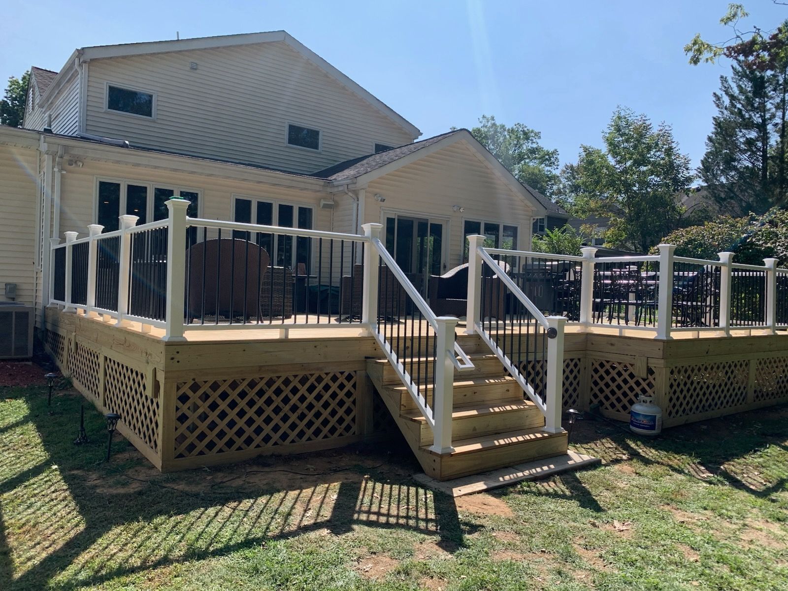 Back deck with stairs, white railings, and lattice skirting on a beige house in a sunny yard