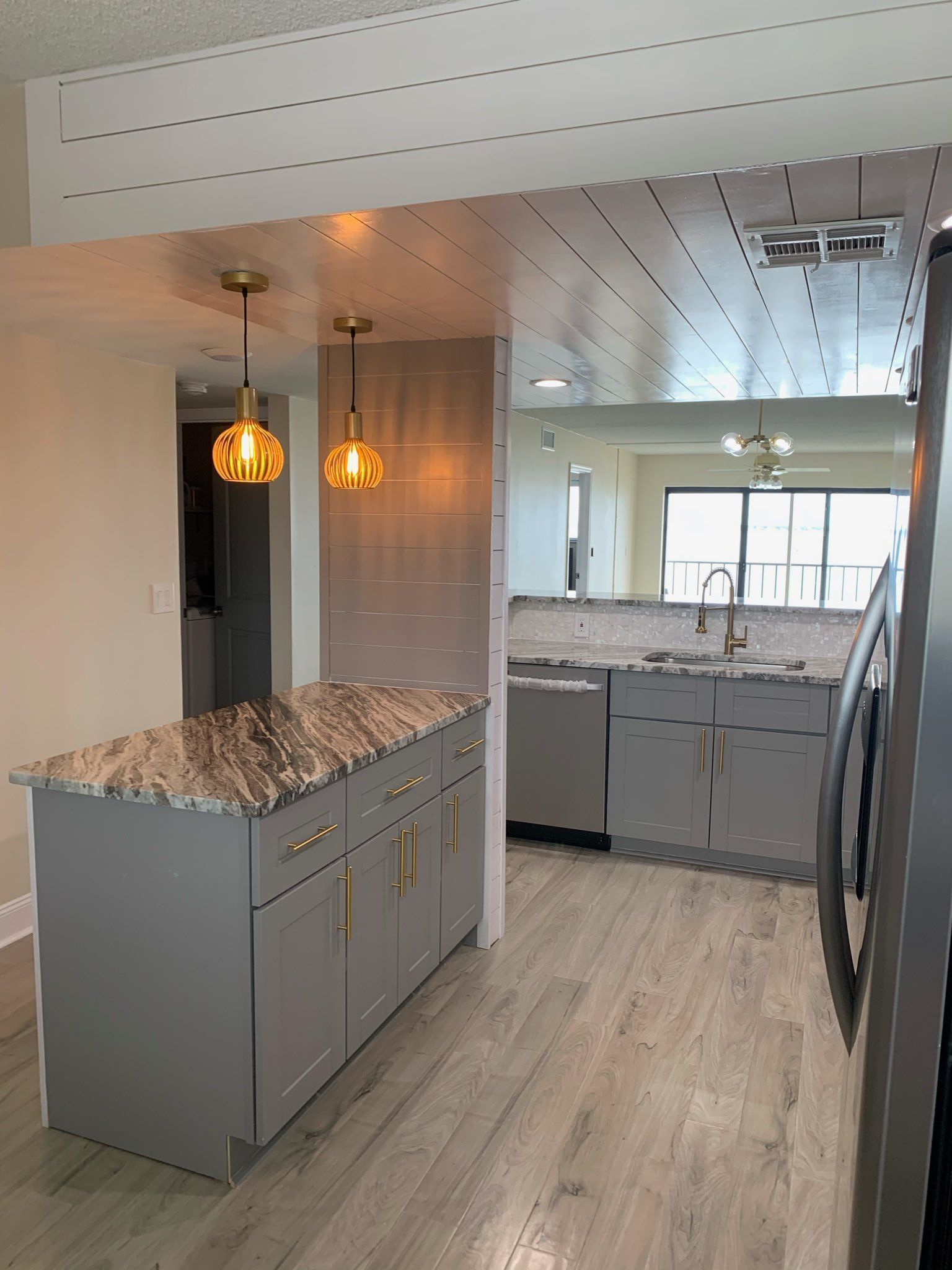 Modern kitchen with gray cabinets, marble countertops, and pendant lights visible through a doorway