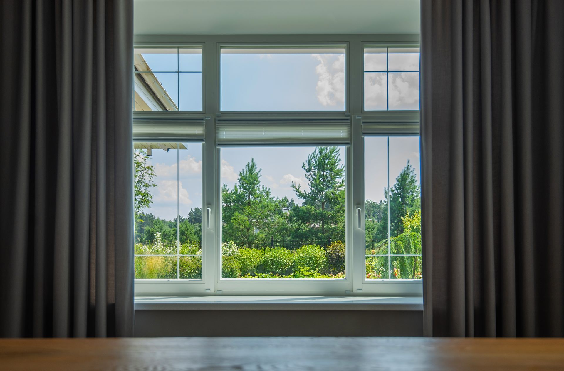 Modern room with large window, gray curtains, and a green garden view outside.
