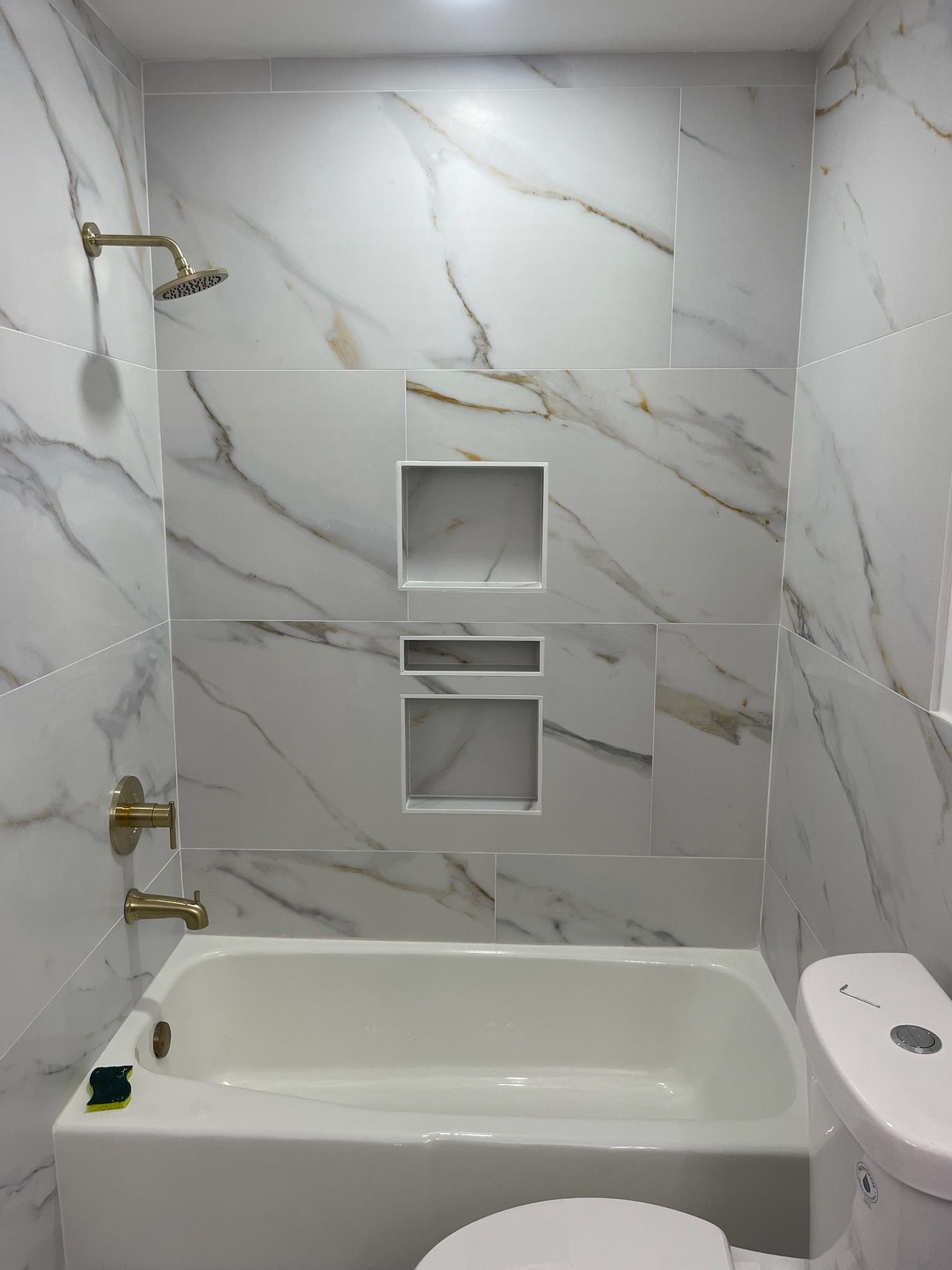 Tiled shower with brass fixtures, built-in niches, and a white bathtub beneath.