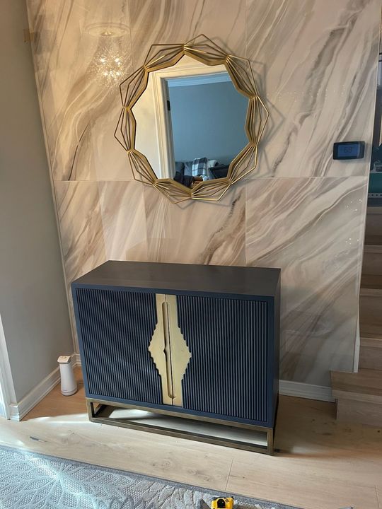 Decorative hallway cabinet with gold-framed mirror above, dark striped doors, and beige walls