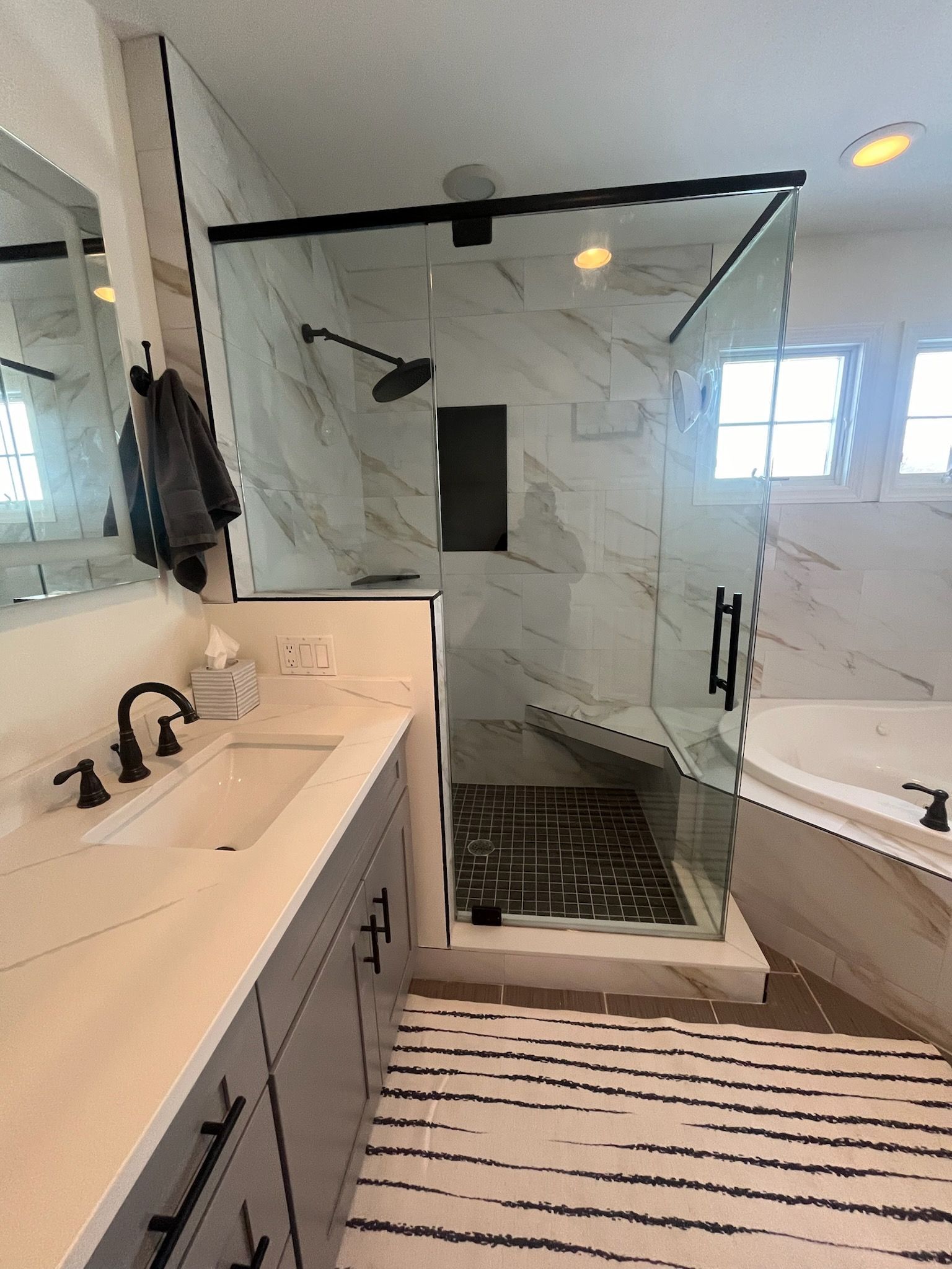 Modern bathroom with double vanity, glass shower, marble walls, and black fixtures