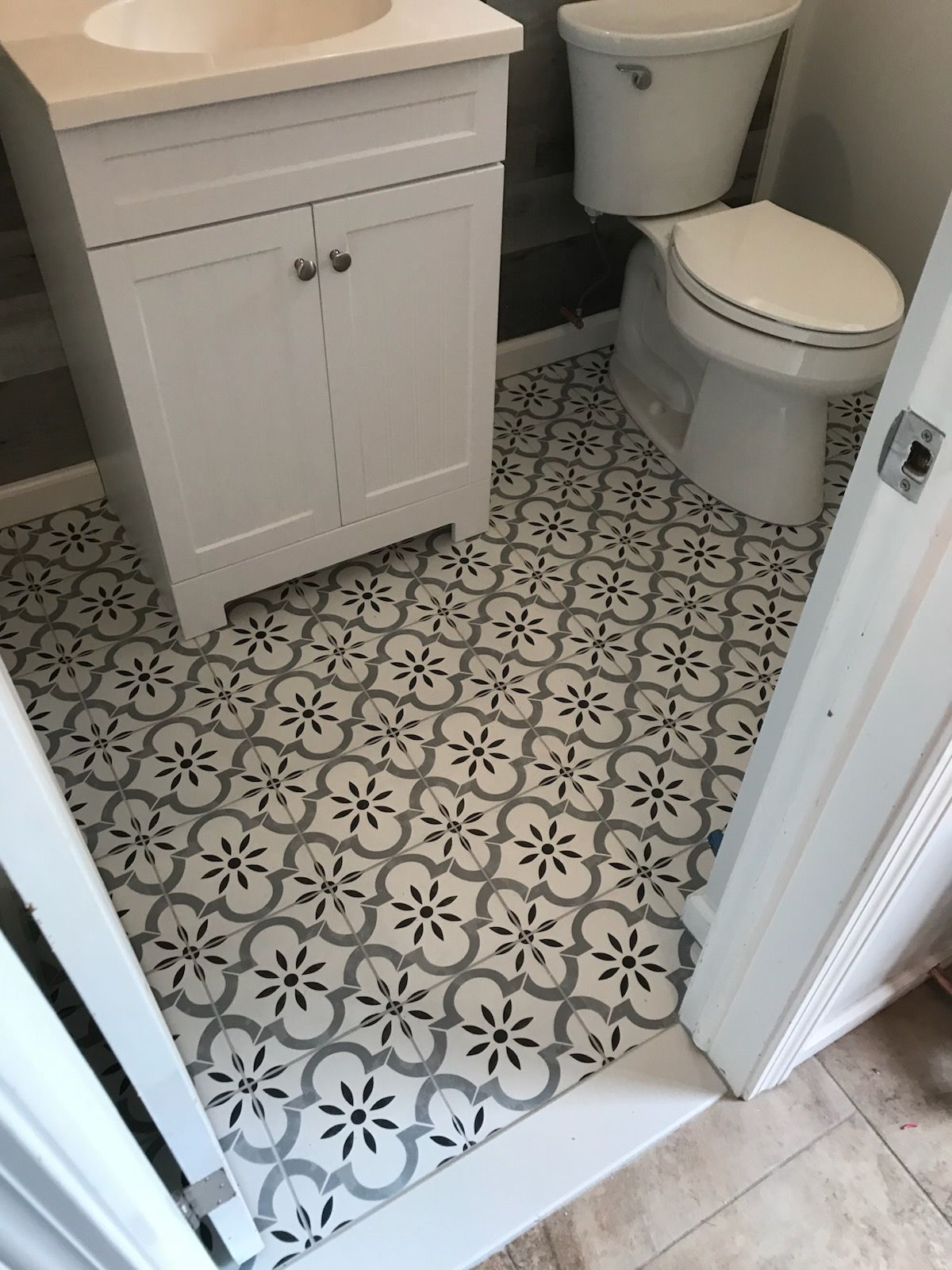 Small bathroom with patterned black-and-white tile floor, white vanity, and toilet.