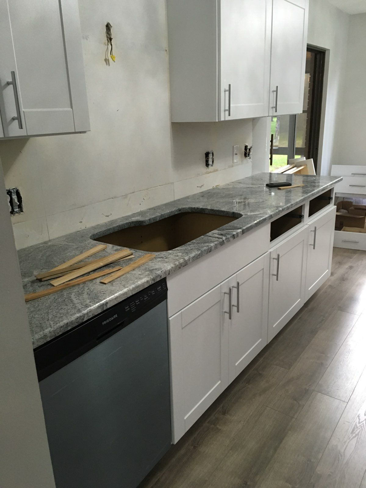 Kitchen under renovation with white cabinets, granite countertop, sink cutout, and dishwasher installed