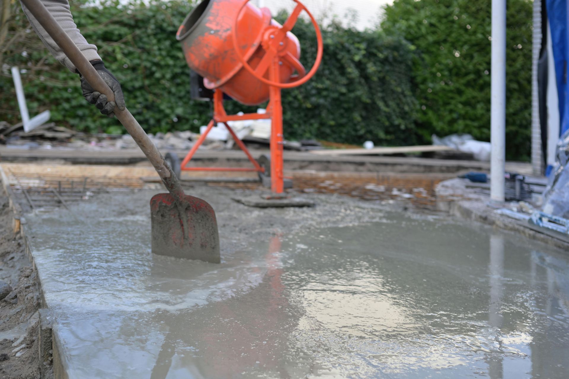 Worker smoothing wet concrete with a shovel, orange cement mixer in the background. Worker smoothing wet concrete with a shovel, orange cement mixer in the background.