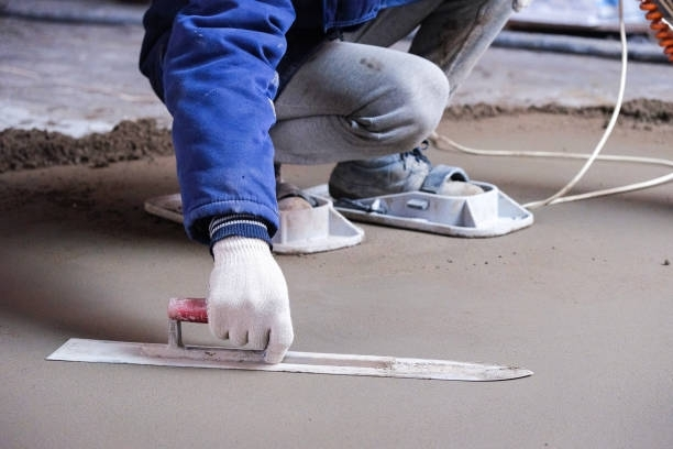 Concrete contractor smoothing wet cement floor with steel trowel during professional slab finishing.