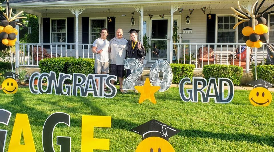 A group of people are standing in front of a house decorated for a graduation party.