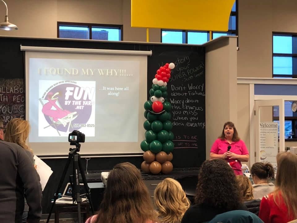 Woman presenting with slideshow, balloon Christmas tree, and audience.