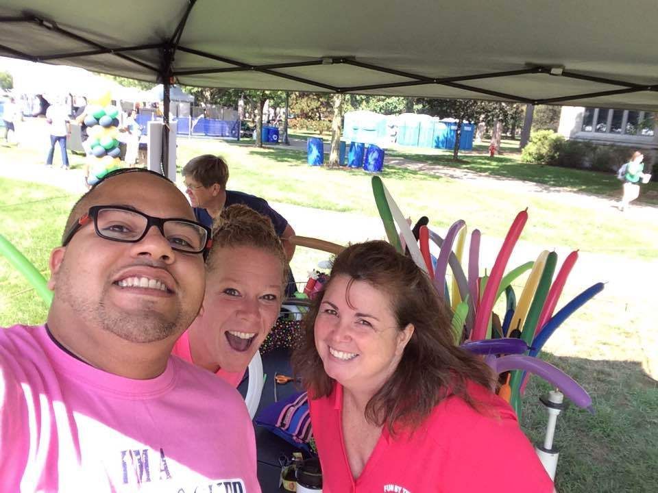 A man and two women are posing for a picture under a tent. Balloon Twisting Entertainment