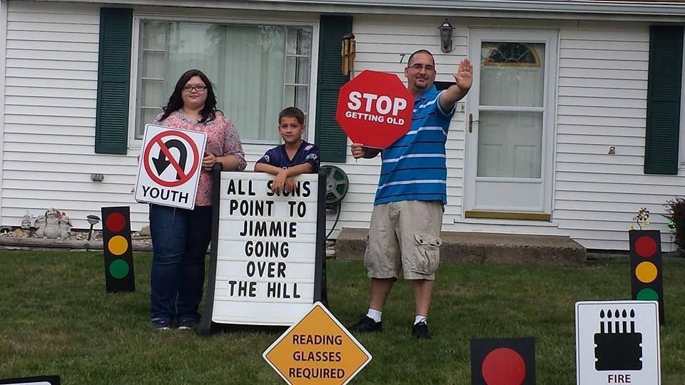 A family standing in front of a house holding signs that say all signs point to jimmie going over the hill
