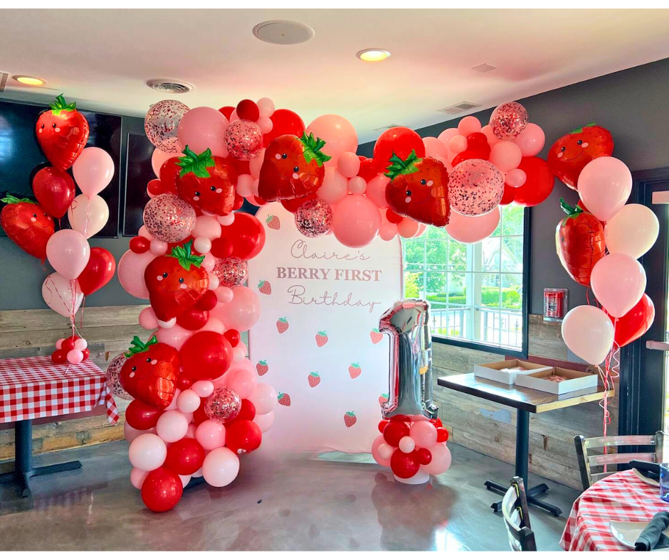 Strawberry-themed first birthday party. balloon arch with strawberry balloons, backdrop, and number 1 balloon.