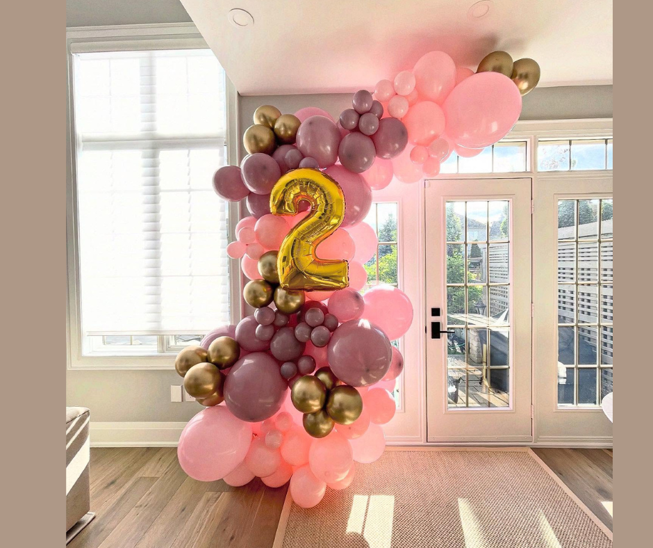 Balloon garland with pink, gold, and purple balloons framing a doorway, gold number