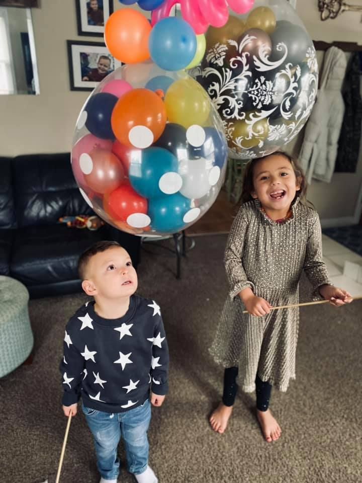 A boy and a girl are holding balloons in a living room.