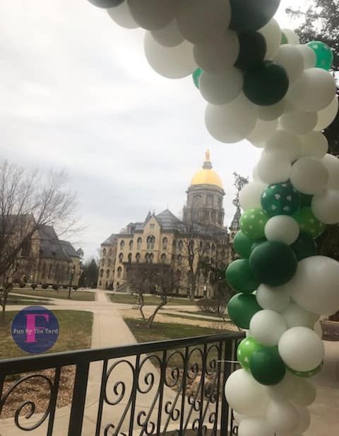 a bunch of green and white balloons are hanging from a fence
