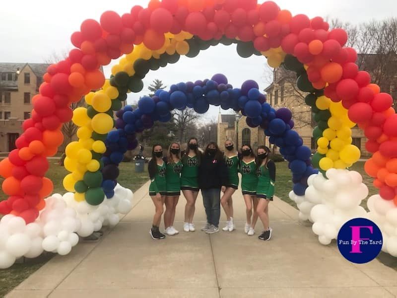 Notre Dame cheerleaders pose with a fun by the yard rainbow balloon arch