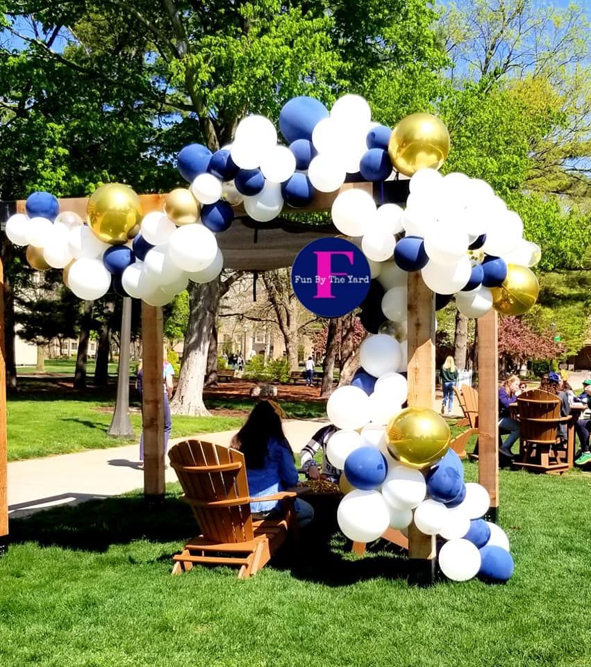 A woman sits in a chair under an arch decorated with blue and white balloons