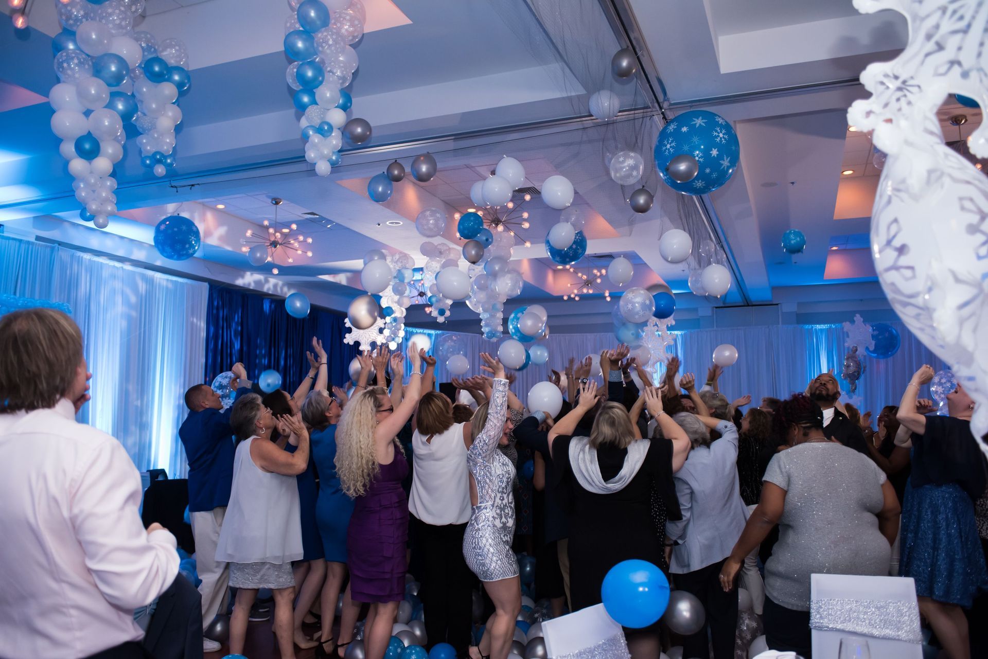 A large group of people are dancing in a room with balloons hanging from the ceiling. Balloon Dorp